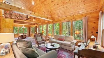 A log cabin interior with a living room, dining area, and large windows.