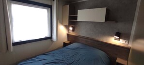 Ein Zimmer mit einem Bett, einem Fenster, einem an der Wand befestigten Regal und Nachttischlampen.