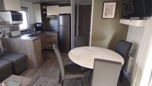 A compact kitchenette with a microwave, toaster, and refrigerator. There is a small dining area with a table and chairs. - Siblu 4* Capbreton 3-Bedroom Solar-Powered Mobile Home — Available (Capbreton)