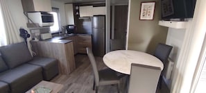 Eine kompakte Küchenzeile mit Mikrowelle, Toaster und Kühlschrank. Es gibt einen kleinen Essbereich mit Tisch und Stühlen.