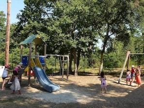 A playground with a slide and climbing structures, surrounded by trees. - Siblu 4* Capbreton 3-Bedroom Solar-Powered Mobile Home — Available (Capbreton)