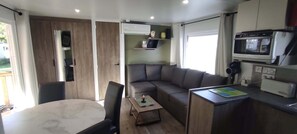 Ein kompakter Wohnbereich mit einer Couch, einem kleinen Tisch, einer Küchenzeile mit einer Mikrowelle und einem Fenster.