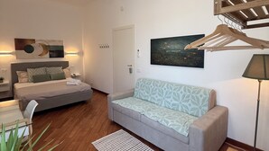 A modern living room with a sofa, a wooden table, a hanging clothes rack, and a bed with a headboard.
