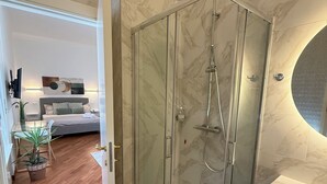 A modern bathroom with a glass-enclosed shower, a marble-tiled wall, and a round mirror.