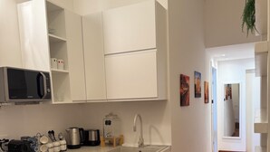 A compact kitchen with white cabinets, a microwave, a sink, and a small bar area with stools.