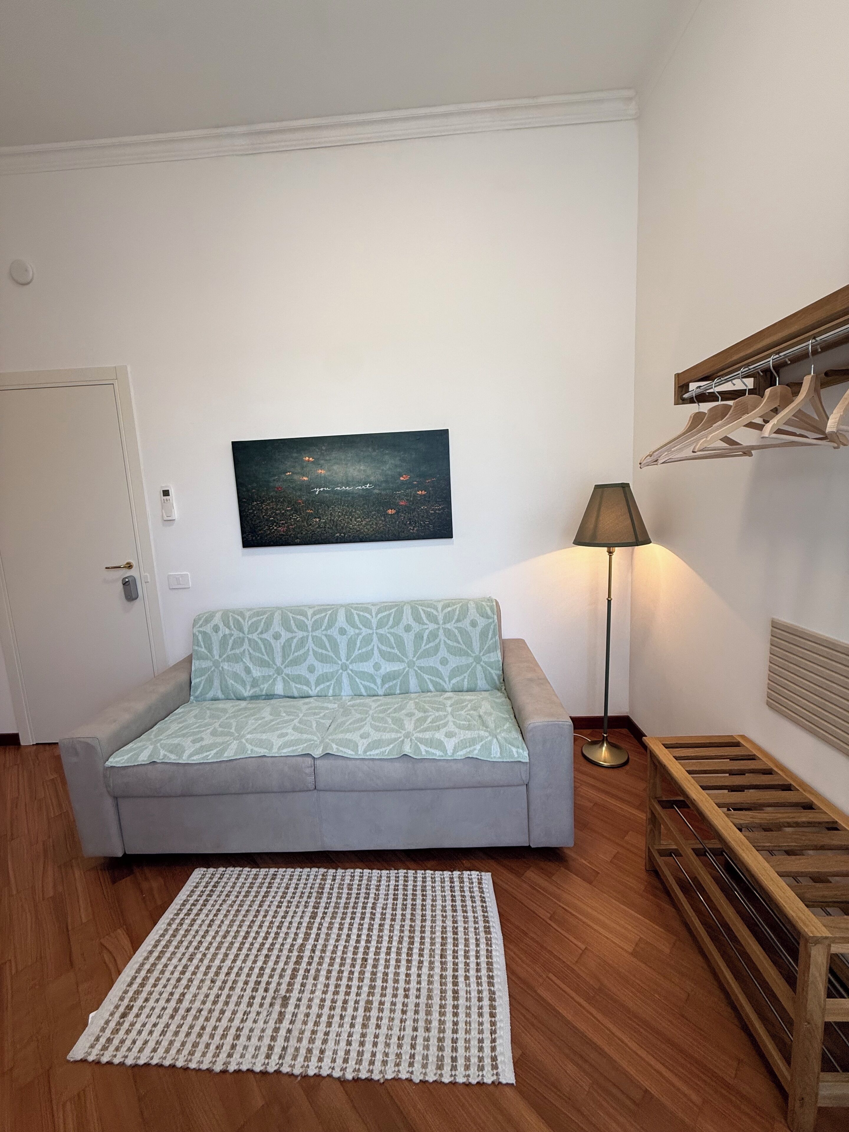 Una sala de estar con un sofá gris, un plaid estampado, una obra de arte enmarcada, una lámpara de pie y un banco de madera.