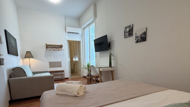 A hotel room with a bed, a sofa, a desk, a television, and a window.
