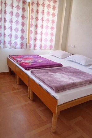 A single bed with a wooden frame, a purple blanket, and a floral-patterned bedspread.