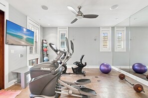 A home gym with exercise equipment, a ceiling fan, and a beach-themed painting. - New Rental, WaterColor, Golf Cart, Resort Amenities (Santa Rosa Beach)