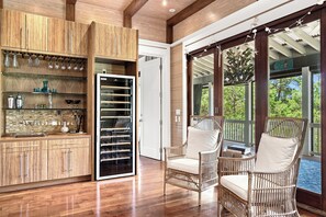 A spacious room with wooden cabinetry, a built-in wine rack, wicker chairs, and a large window offering a view of the outdoors. - New Rental, WaterColor, Golf Cart, Resort Amenities (Santa Rosa Beach)