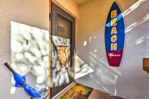 Eine Tür mit Fenster, ein blauer Regenschirm und ein Schild mit Surfbrett-Motiv und dem Schriftzug 'BEACH House'.