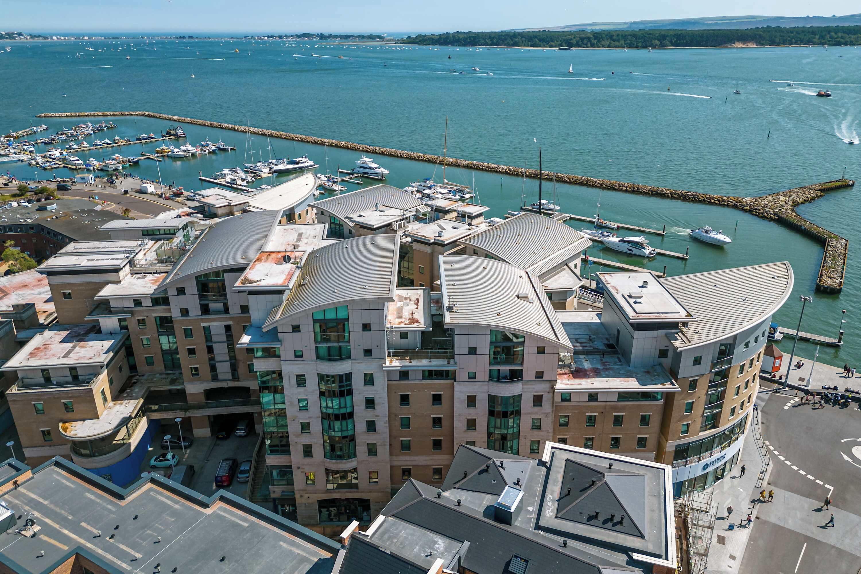 A modern hotel with a curved roof, located near a marina with boats.