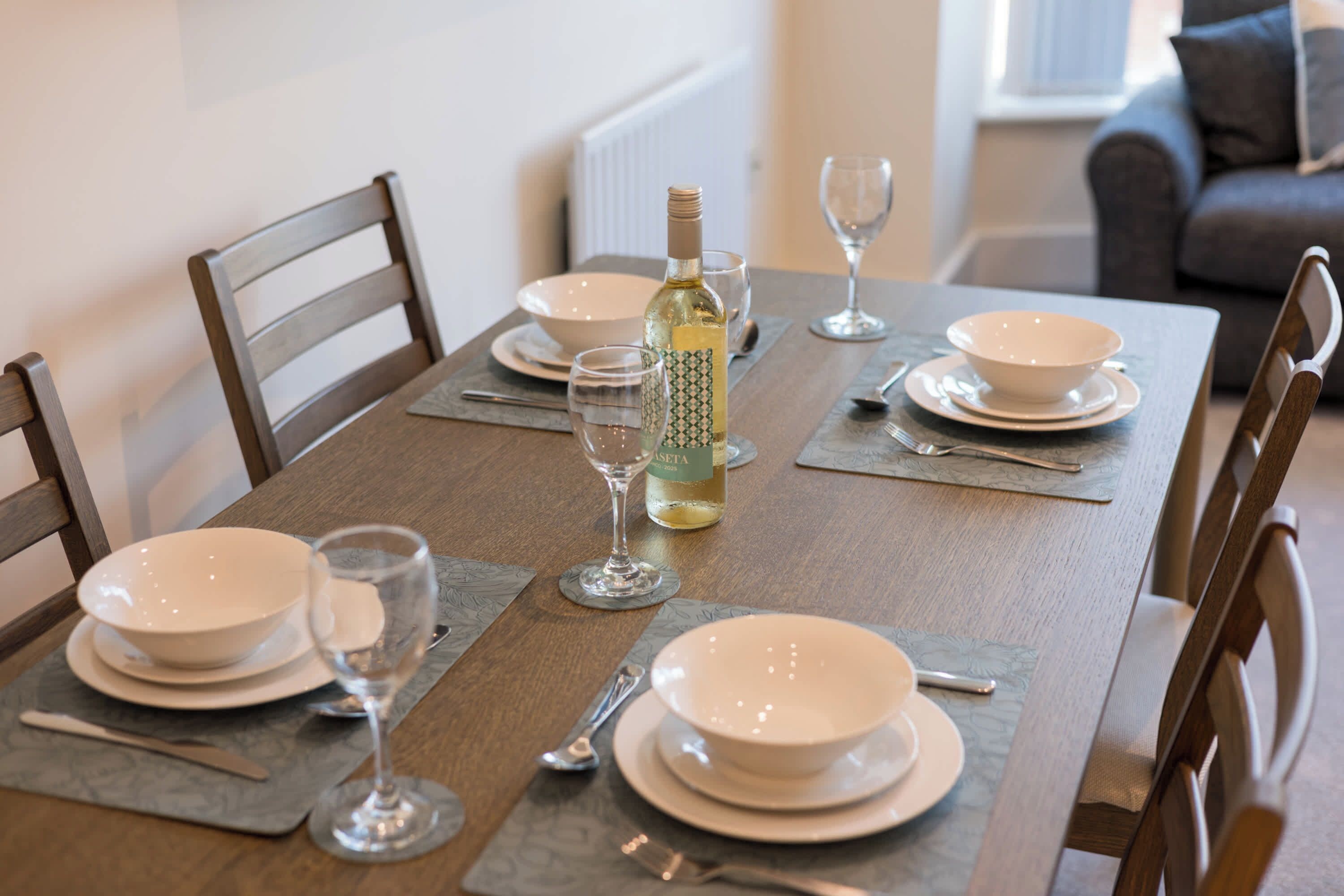 A dining table set with plates, glasses, cutlery, and a bottle of wine.