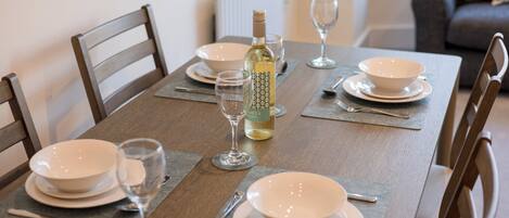 A dining table set with plates, glasses, cutlery, and a bottle of wine.