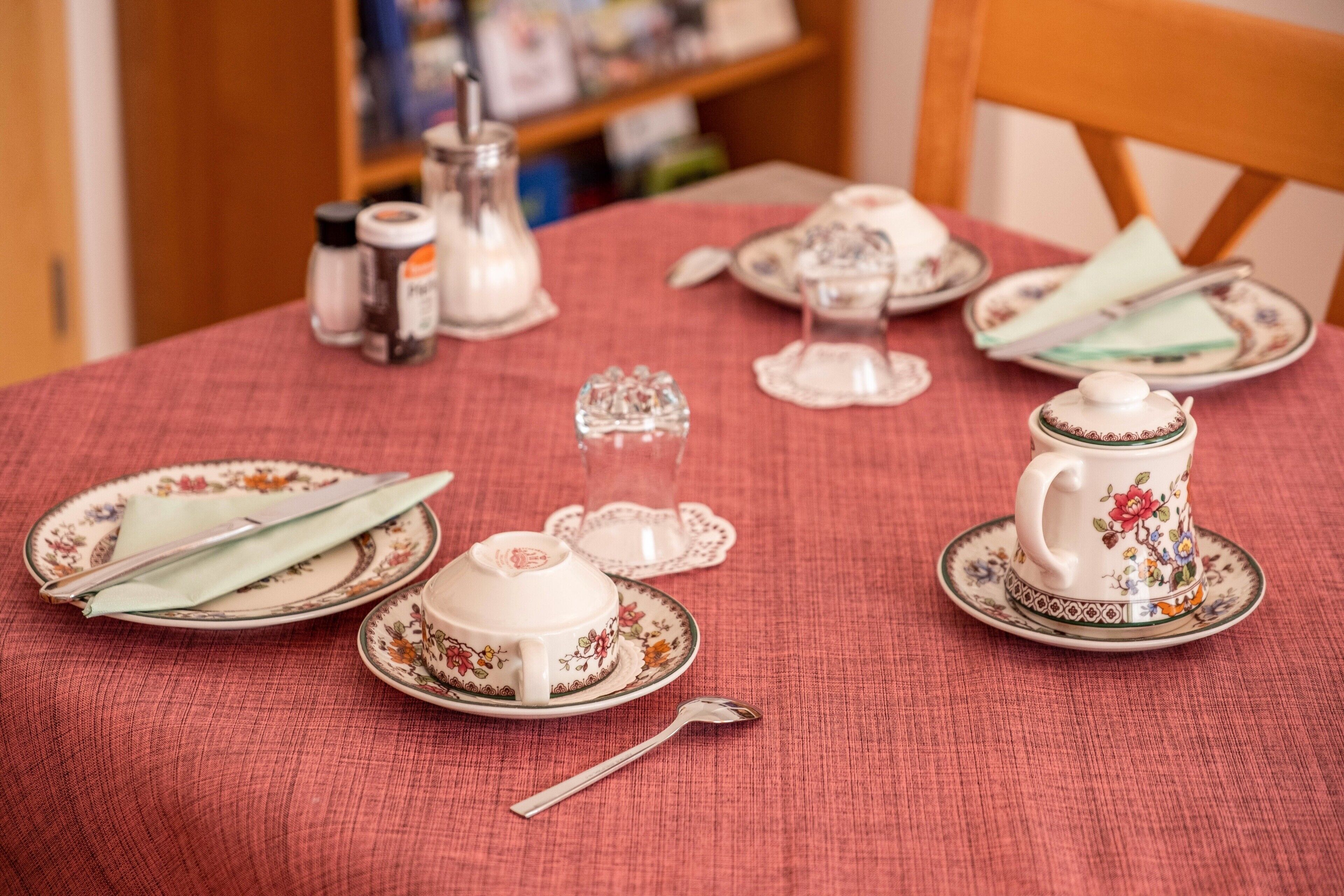 A dining table with a floral tablecloth, a teapot, cups, and a sugar bowl.