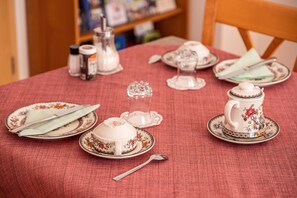 A dining table with a floral tablecloth, a teapot, cups, and a sugar bowl.