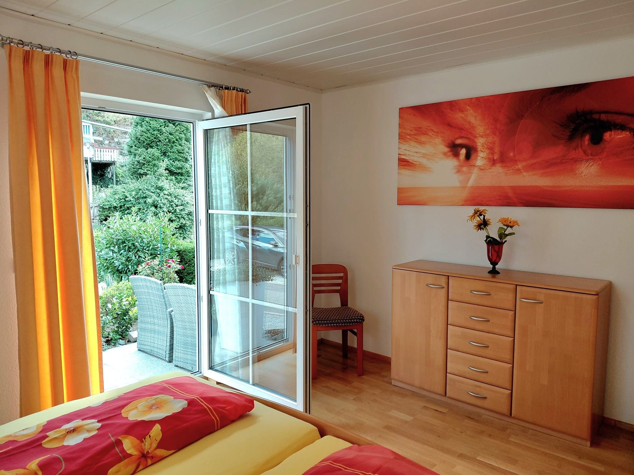 Quarto com porta de vidro deslizante para uma varanda, um armário de madeira e um quadro na parede.