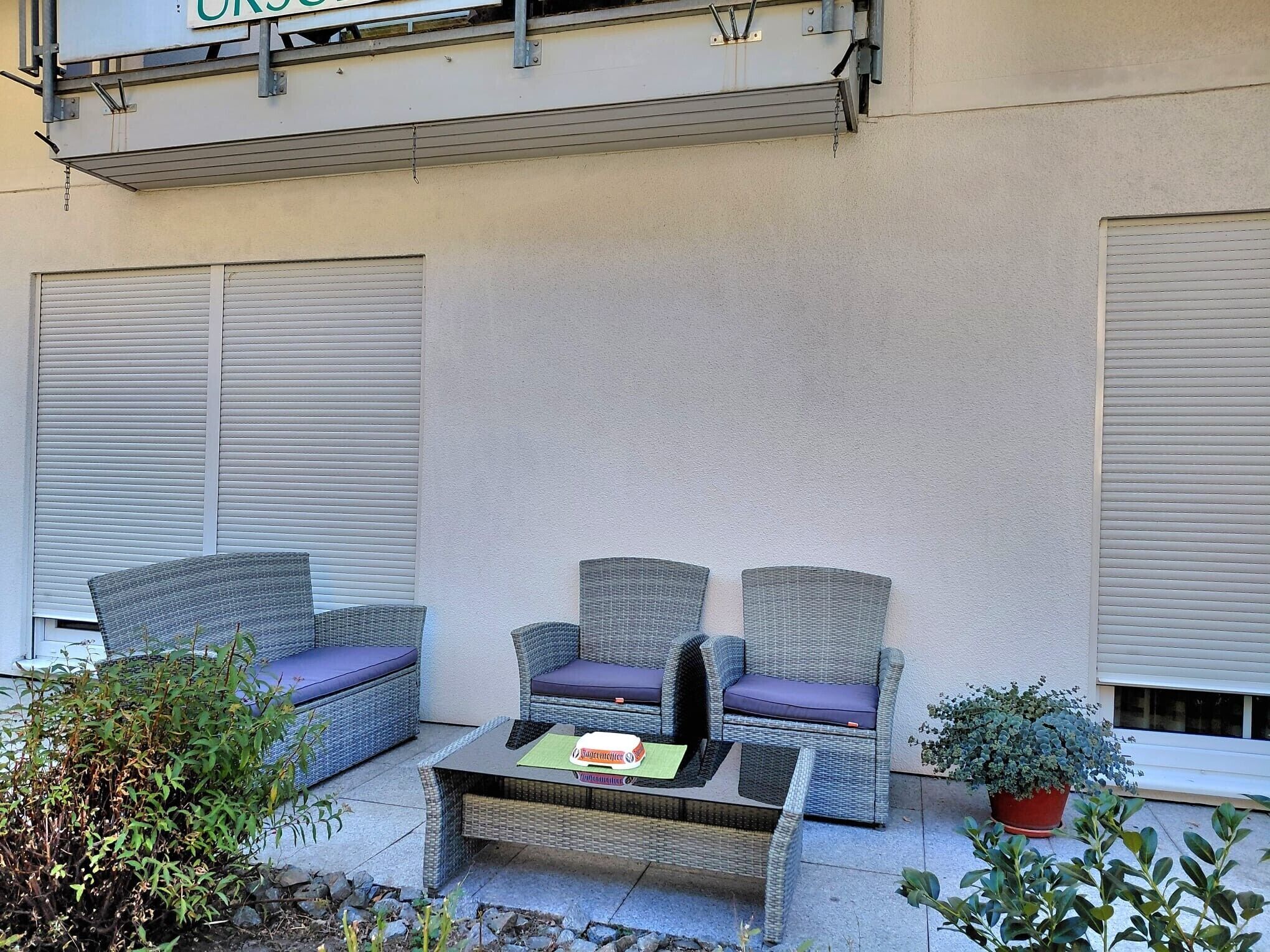A patio with wicker furniture and a table, surrounded by potted plants.