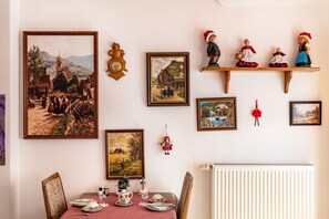 Ein Essbereich mit Tisch für zwei Personen, umgeben von verschiedenen gerahmten Kunstwerken und einem Holzboden mit Figuren.