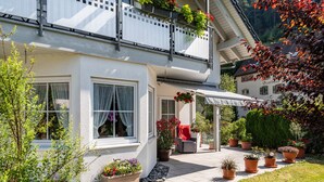 Una casa blanca amb un balcó, plantes en testos i una zona de pati coberta.