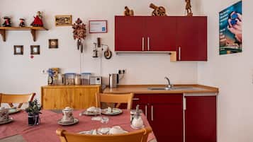 A compact kitchen with wooden cabinets, a dining table set with dishes, and a red refrigerator.