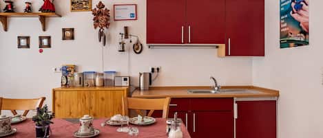 A compact kitchen with wooden cabinets, a dining table set with dishes, and a red refrigerator.