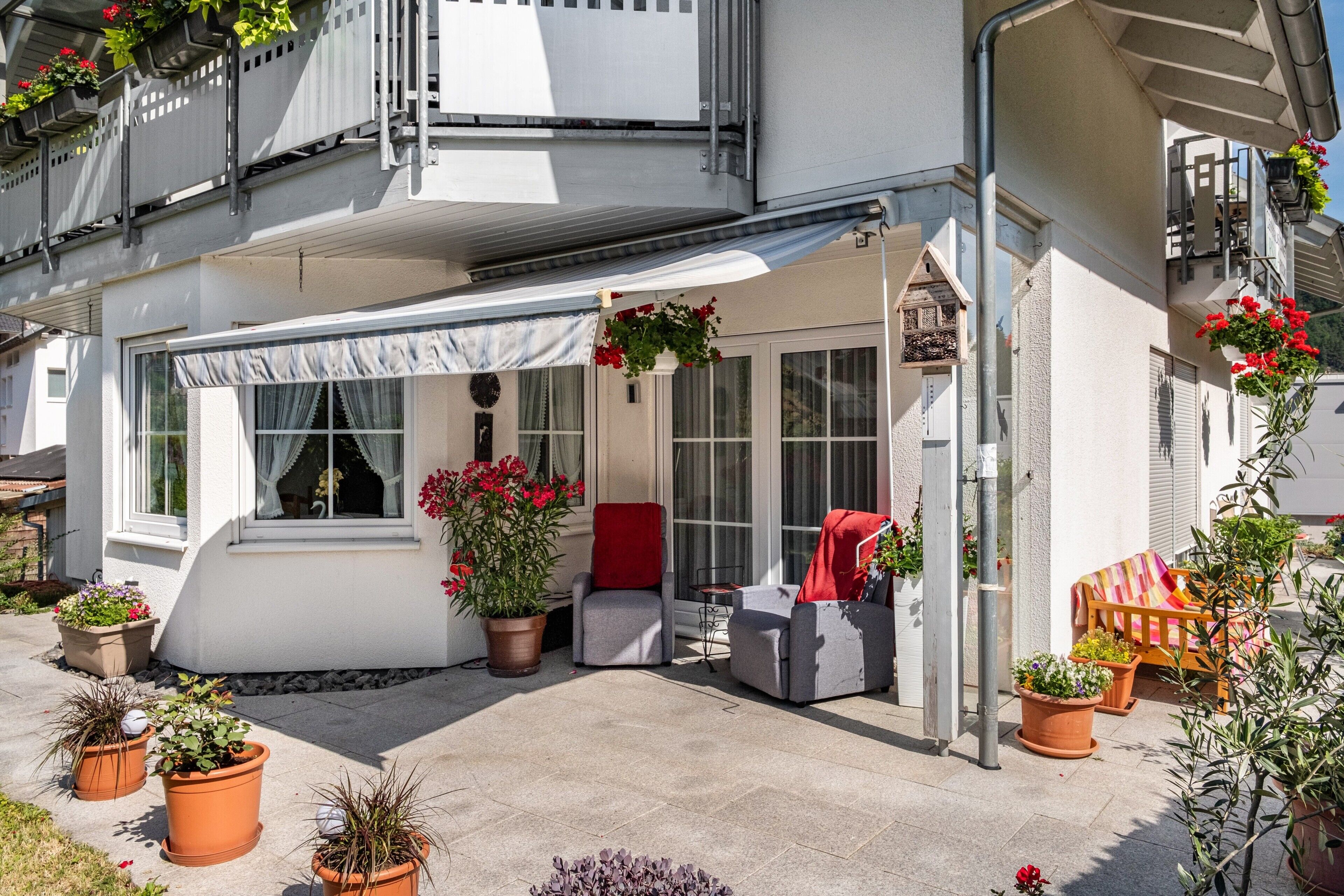 A covered outdoor seating area with potted plants and a red chair.