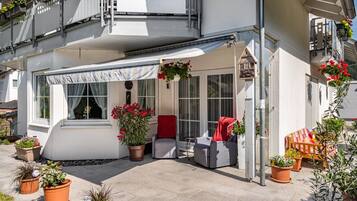 A covered outdoor seating area with potted plants and a red chair.