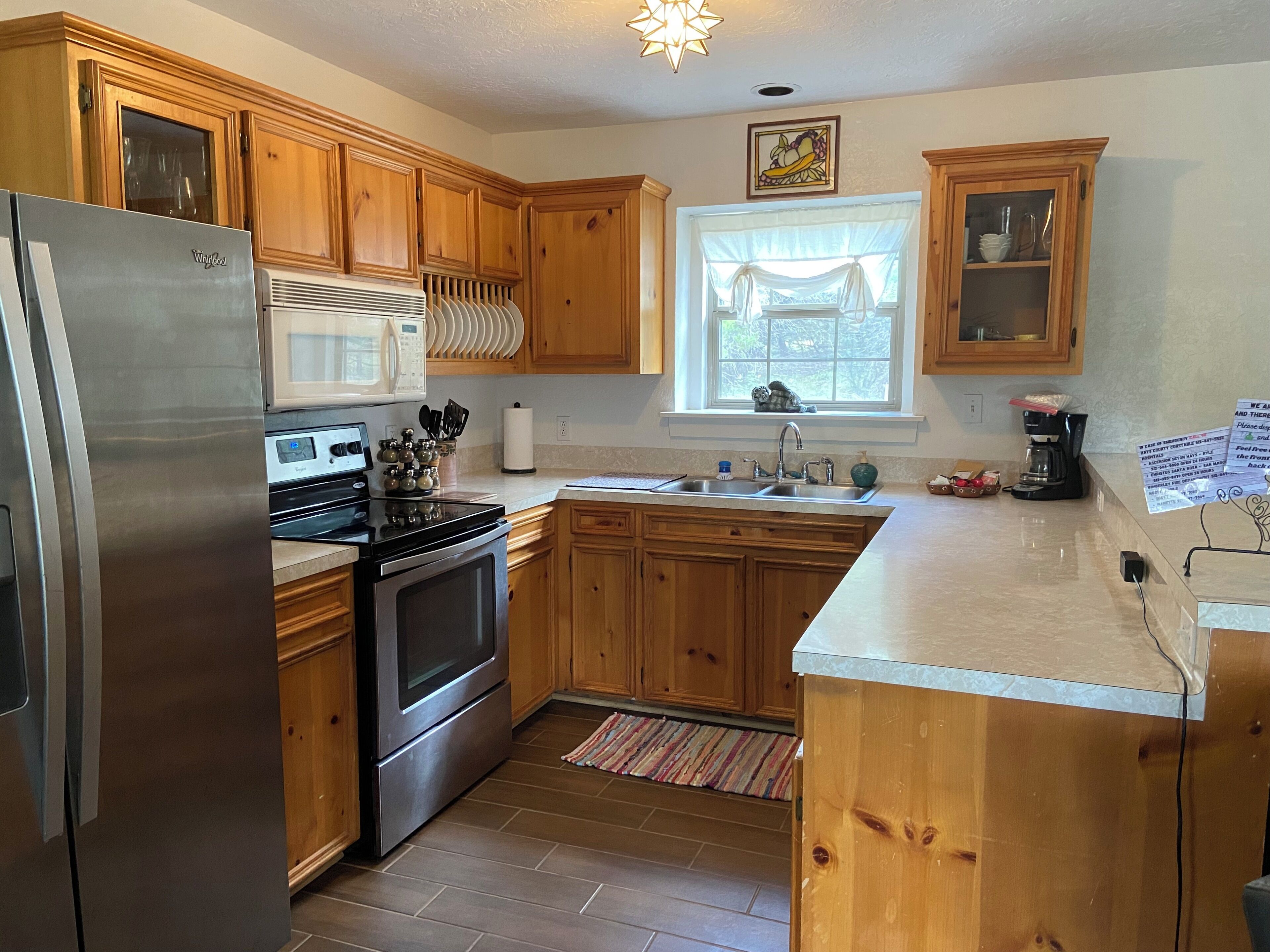 A kitchen with wooden cabinets, a stainless steel refrigerator, a microwave, an oven, and a window with curtains.