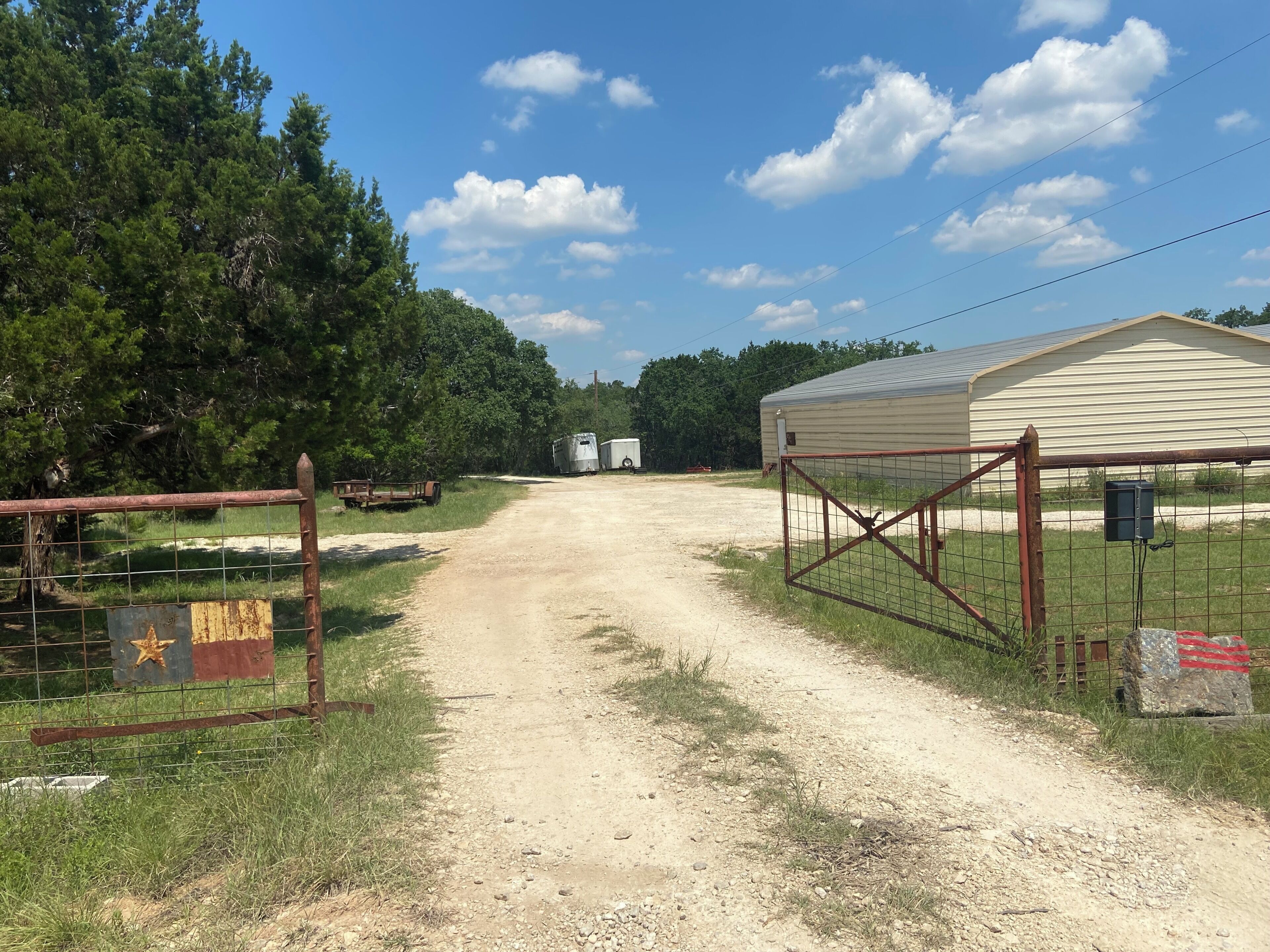 A rural road leading to a gated area with a barn and trailers.