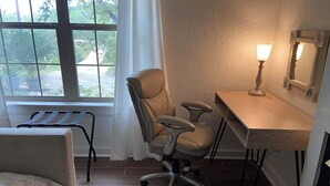 Ein Zimmer mit Schreibtisch, Stuhl und einem Fenster mit Blick ins Grüne.