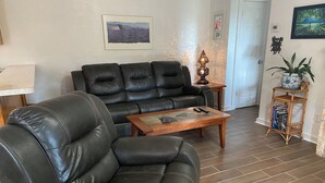 Ein Wohnzimmer mit einem schwarzen Ledersofa, einem Holztisch als Couchtisch und einem kleinen Beistelltisch mit Lampe.