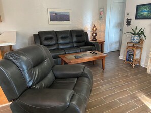 Ein Wohnzimmer mit einem schwarzen Ledersofa, einem Holztisch als Couchtisch und einem kleinen Beistelltisch mit Lampe.