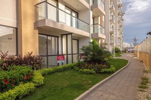 Un moderno edificio de apartamentos con balcones, entrada porticada y un jardín ajardinado.