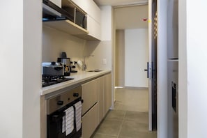A compact kitchen with a stove, microwave, and oven, a small countertop, and a door leading to another room. - Coralina Suites: ¡Tu Refugio en Santa Marta! (Santa Marta)