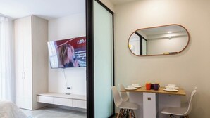 Un salon moderne doté d’un téléviseur à écran plat, d’un coin repas avec une table et des chaises en bois, d’un banc et d’un miroir mural.
