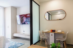 A modern living room with a flat-screen TV, a dining area with a wooden table and chairs, a bench, and a mirror on the wall. - Coralina Suites: ¡Tu Refugio en Santa Marta! (Santa Marta)