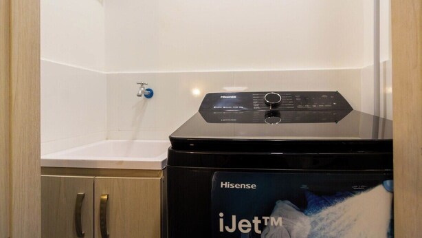 Une machine à laver Hisense iJetTM dans une salle de bain avec un lavabo blanc et des meubles en bois.
