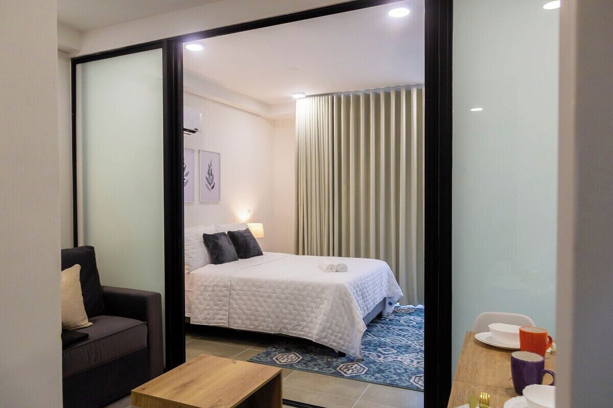 A hotel room with a bed, a sofa, a wooden table, and a dining area with chairs and a table.