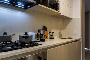 A modern kitchen with a gas stove, two pots, a toaster, a coffee maker, and a sink. - Coralina Suites: ¡Tu Refugio en Santa Marta! (Santa Marta)