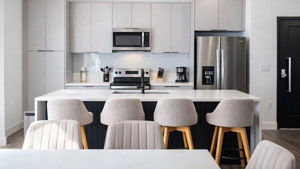 A modern kitchen with white cabinets, stainless steel appliances, and a central island with bar stools. - Kissimmee Villa 5BR Private Pool (Davenport)
