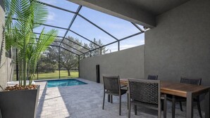 A covered patio area with a pool, a wooden table and chairs, and a potted plant. - Kissimmee Villa 5BR Private Pool (Davenport)