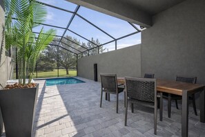 Ein überdachter Patio-Bereich mit Pool, Holztisch und Stühlen sowie einem Topfpflanzen.