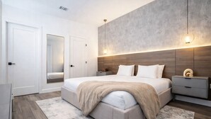A modern bedroom with a large bed, bedside tables, a mirror, and a wall-mounted light fixture. - Kissimmee Villa 5BR Private Pool (Davenport)