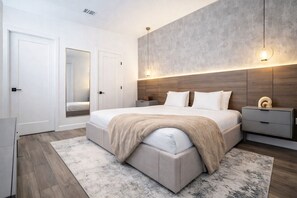 Ein modernes Schlafzimmer mit einem großen Bett, Nachttischen, einem Spiegel und einer Wandleuchte.