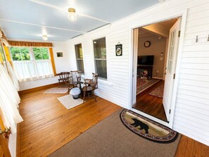 A room with a wooden floor, a dining table with chairs, a television, and a door leading to another room.