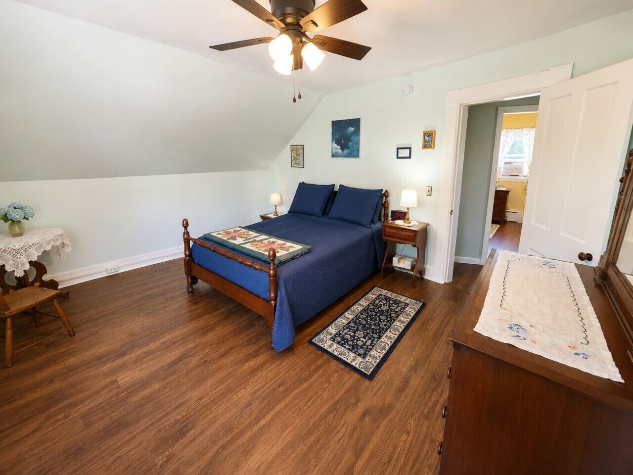 A bedroom with a wooden bed, a ceiling fan, a nightstand, and a night lamp.