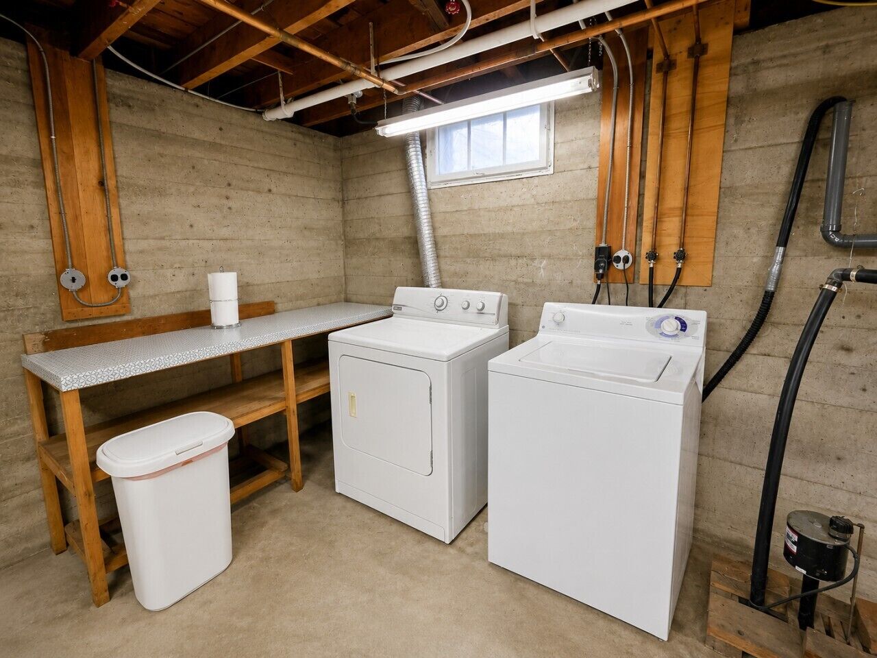 A laundry room with two washing machines, a sink, and a trash bin.
