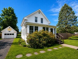 A two-story white house with a garage, a front yard with a bush, and a wooden fence.