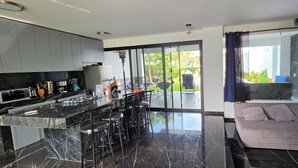 Una cocina moderna con una isla central, taburetes de bar y un área de comedor con vistas al exterior.